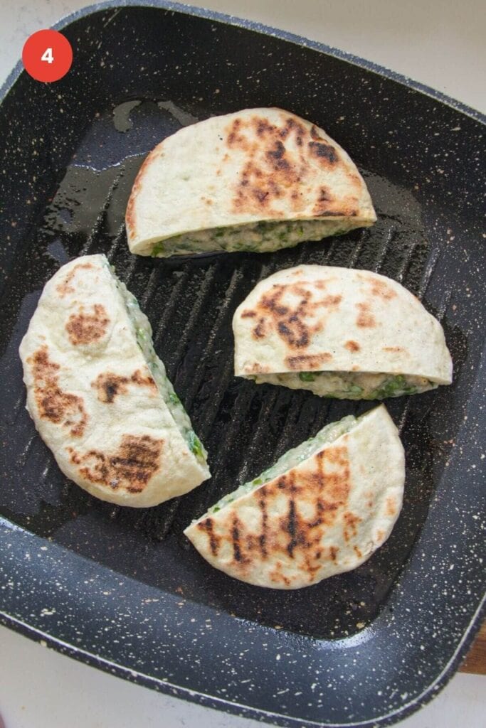 Dumpling stuffed flatbreads cooking in a pan.