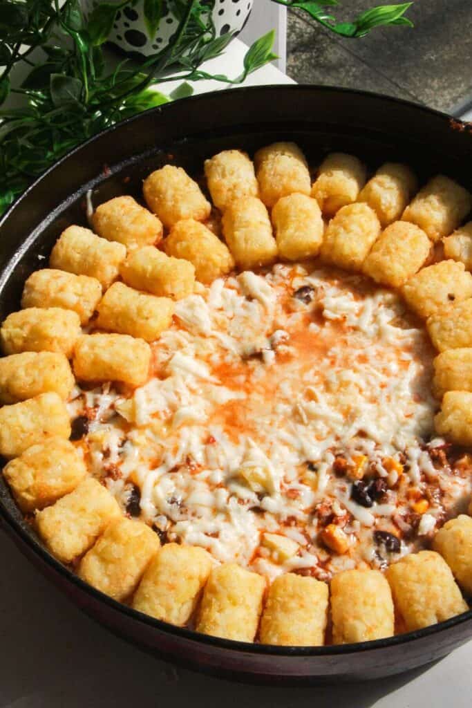 Tater tots being arranged on top of cowboy casserole in a large pan.