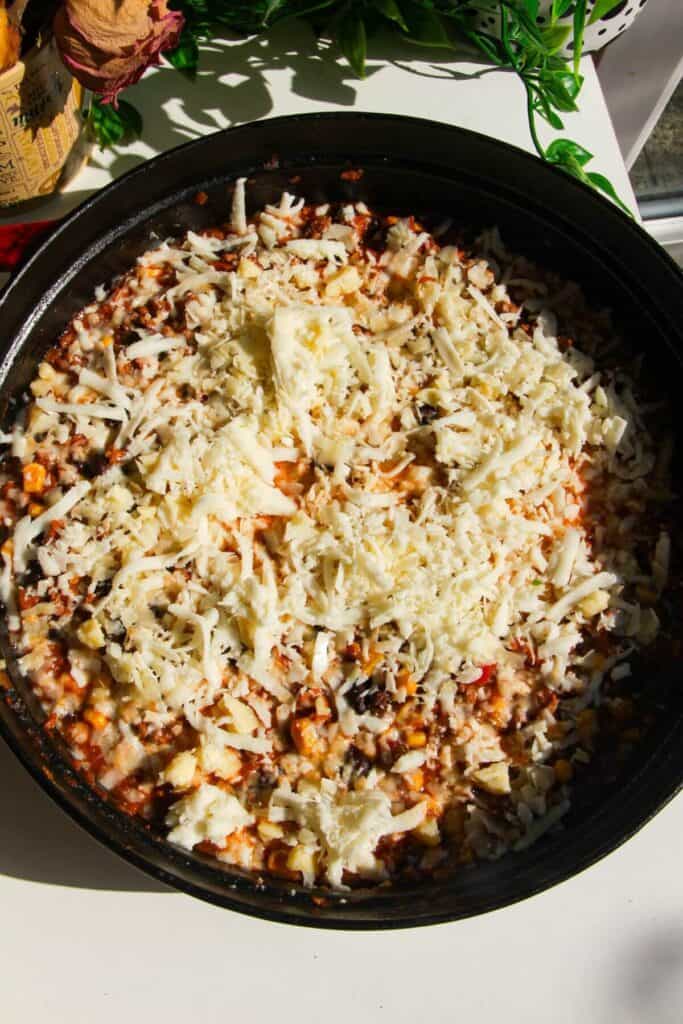 Shredded cheese on top of ground beef in a large pan.