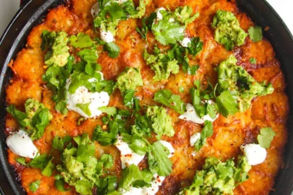 Baked Cowboy Casserole in a large pan with avocado and sour cream on top.