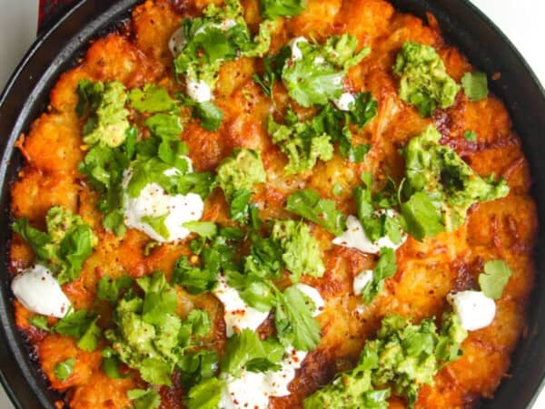 Baked Cowboy Casserole in a large pan with avocado and sour cream on top.