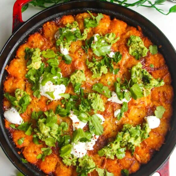 Baked Cowboy Casserole in a large pan with avocado and sour cream on top.