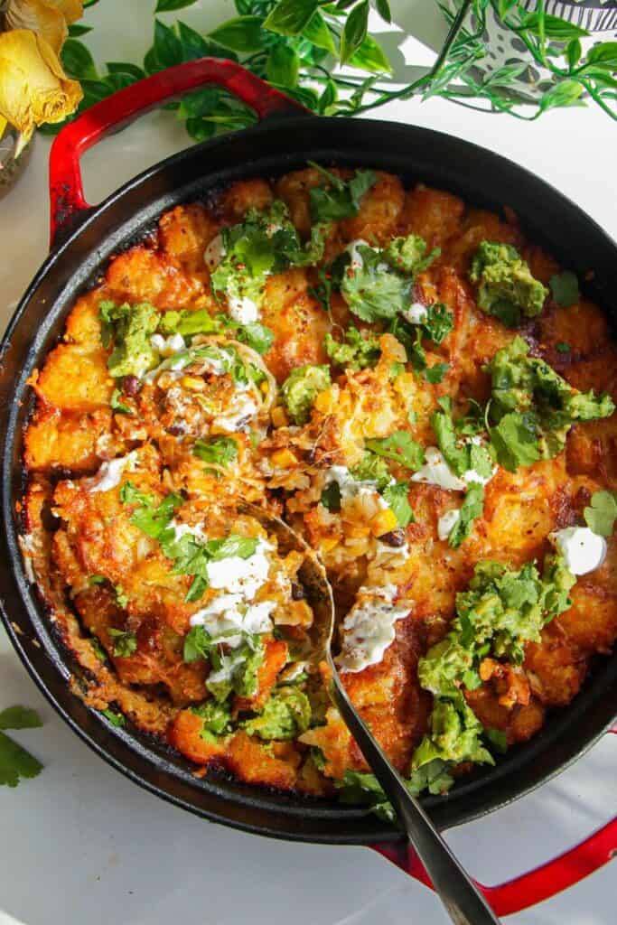 Baked Cowboy Casserole in a large pan with avocado and sour cream on top.