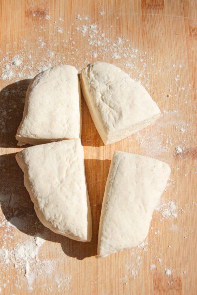 Cottage cheese gnocchi dough cut into quarters on a wooden board.