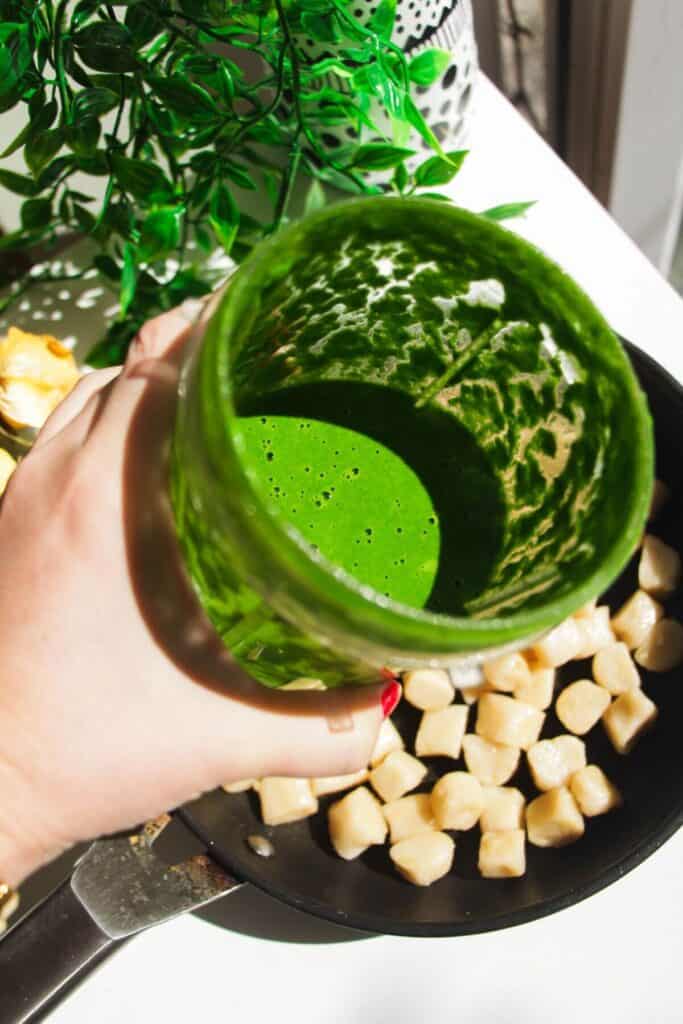 Holding blitzed green goddess sauce over pan of gnocchi.