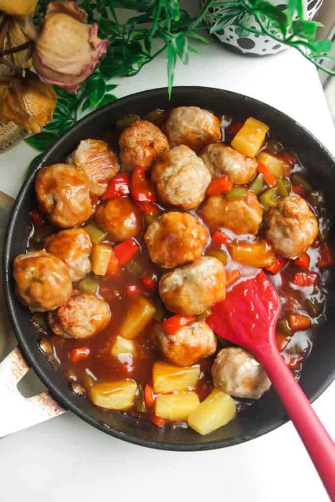 Chicken meatballs added into sweet and sour sauce in a pan.