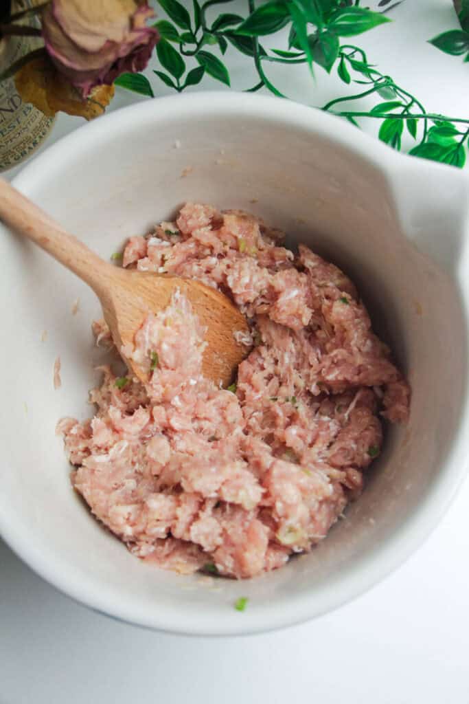 Ground chicken mixed with other meatball ingredients in a bowl.