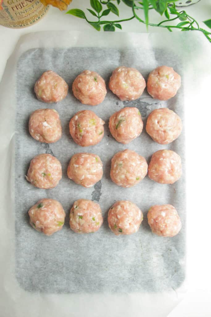 Chicken meatballs on a parchment paper lined oven tray.