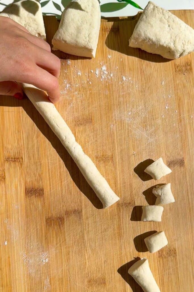 Thin log of gnocchi dough on a wooden board.
