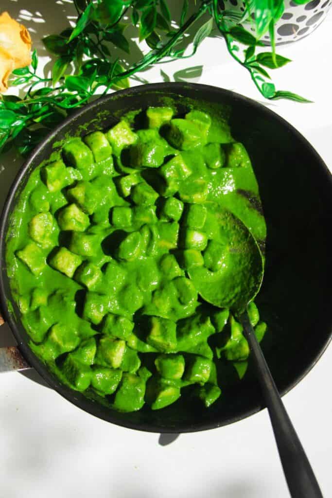Green goddess sauce added to gnocchi in a pan.
