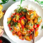 Sweet and sour meatballs over rice in a white bowl.