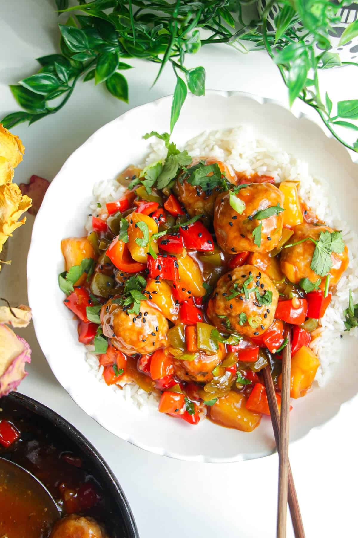 Sweet and sour meatballs over rice in a white bowl.