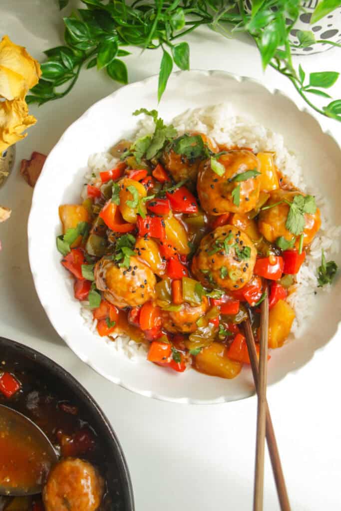Sweet and sour meatballs over rice in a white bowl.