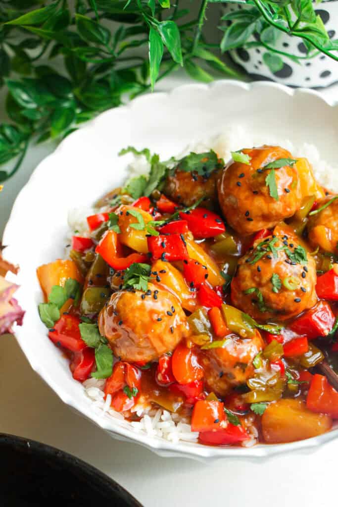 Sweet and sour meatballs over rice in a white bowl.