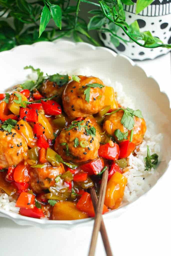 Sweet and sour meatballs over rice in a white bowl.