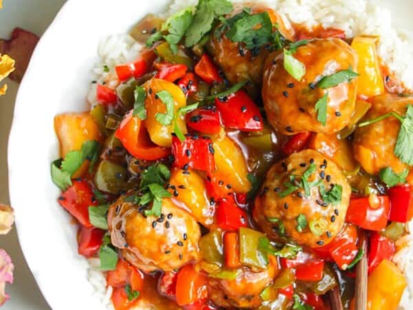 Sweet and sour meatballs over rice in a white bowl.