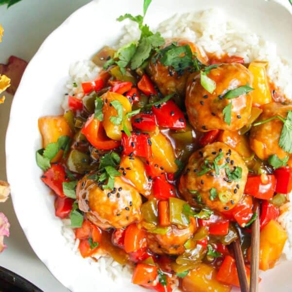 Sweet and sour meatballs over rice in a white bowl.