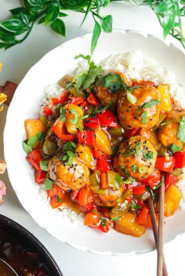 Sweet and sour meatballs over rice in a white bowl.