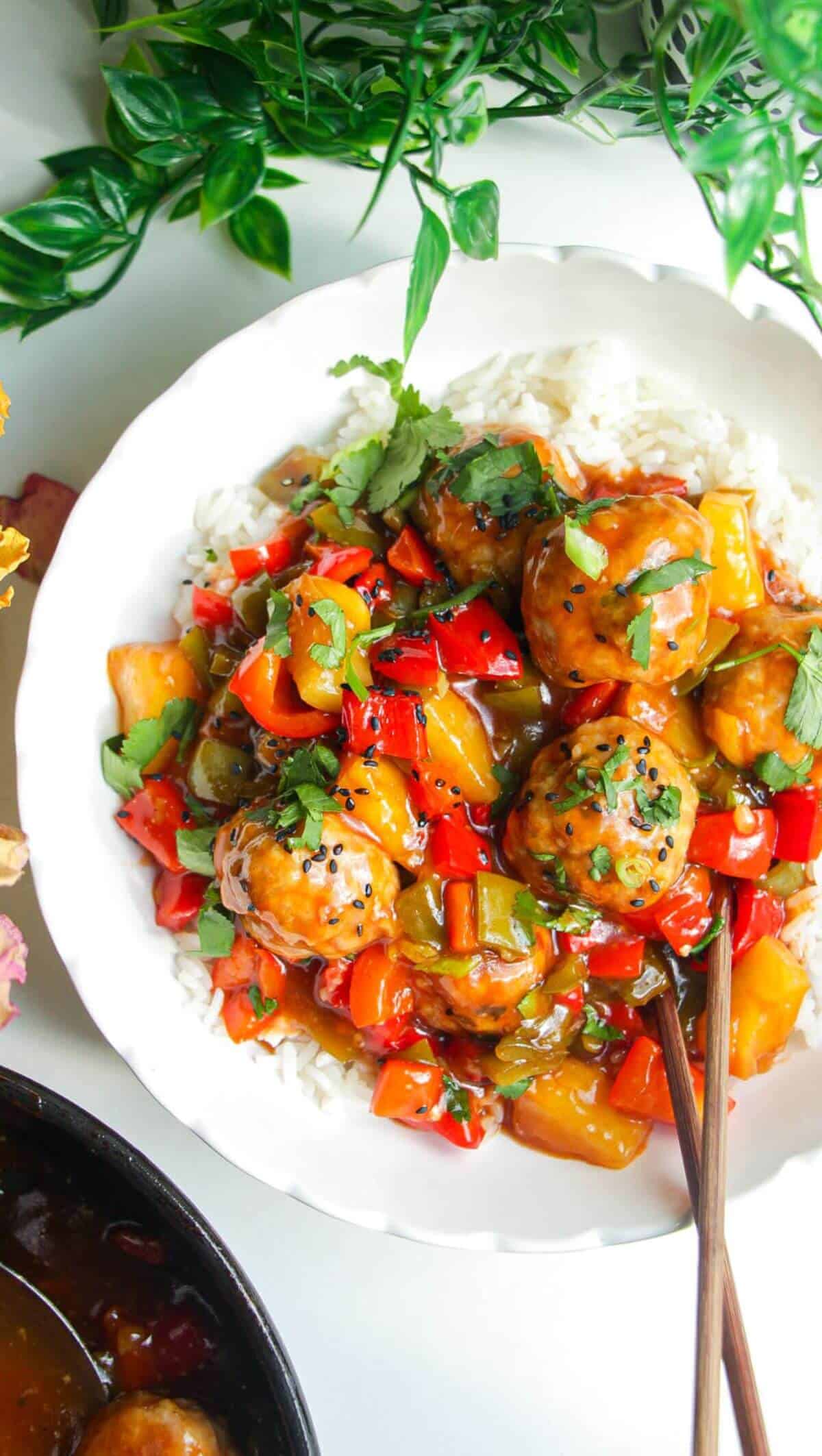Sweet and sour meatballs over rice in a white bowl.