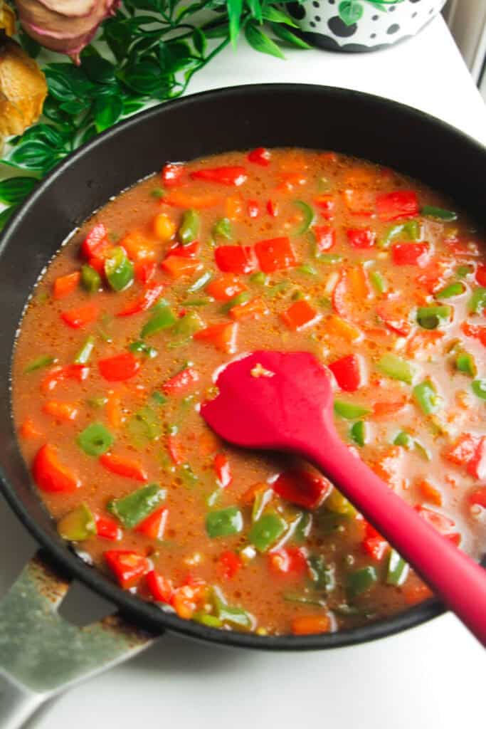 Sauce added to bell peppers in a frying pan.