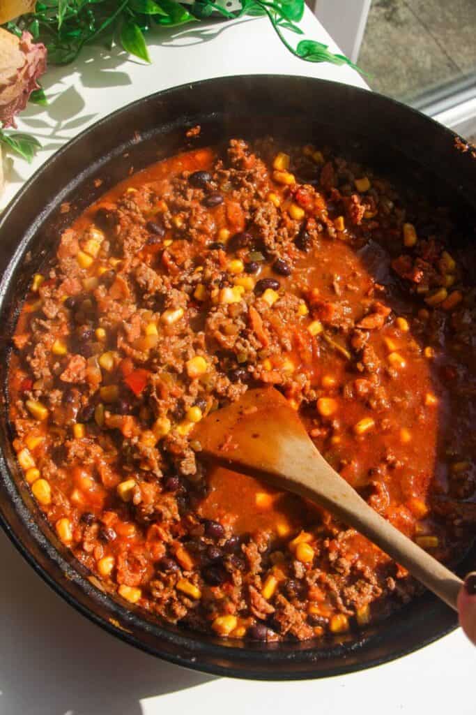 Canned tomatoes, beans and corn added to ground beef in a large pan.