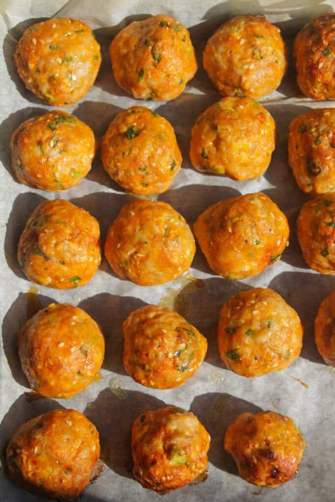 Cooked gochujang meatballs on a lined oven tray.