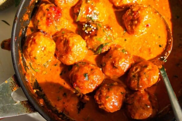 Gochujang chicken meatballs mixed with coconut gochujang sauce in a pan.