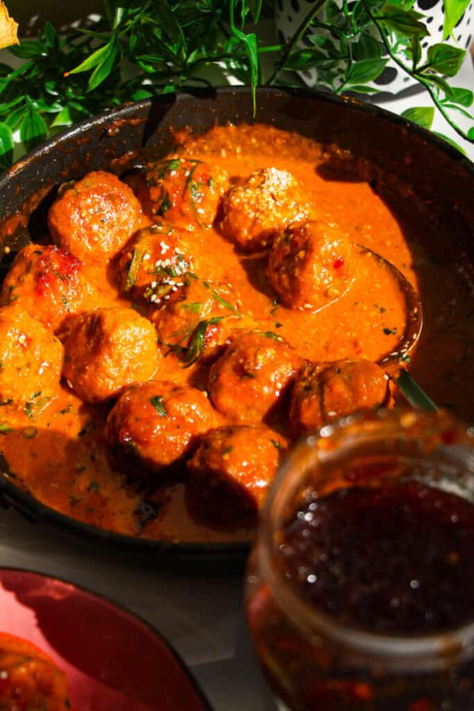 Gochujang chicken meatballs mixed with coconut gochujang sauce in a pan.