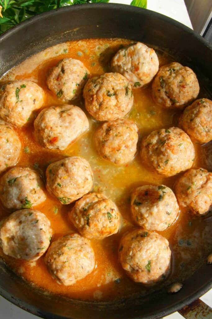Chicken meatballs added to piccata sauce in a pan.