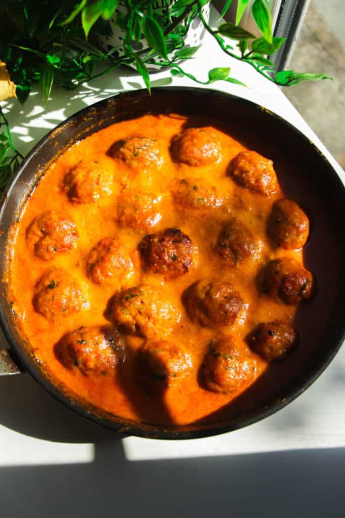 Gochujang chicken meatballs mixed with coconut gochujang sauce in a pan.