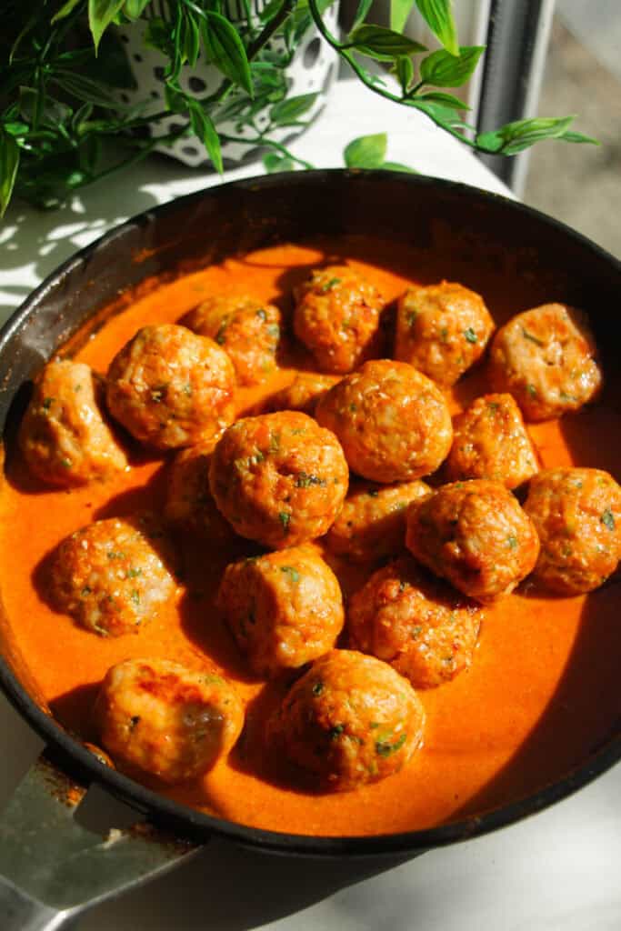 Cooked gochujang chicken meatballs added to coconut gochujang sauce in a pan.