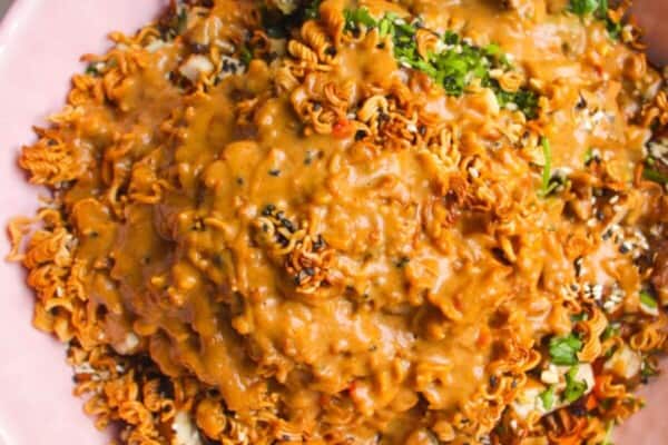 Peanut satay dressing poured over crispy ramen salad in pink bowl.