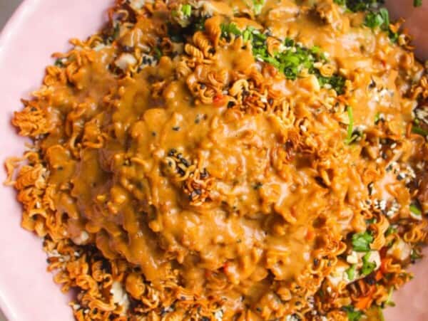 Peanut satay dressing poured over crispy ramen salad in pink bowl.