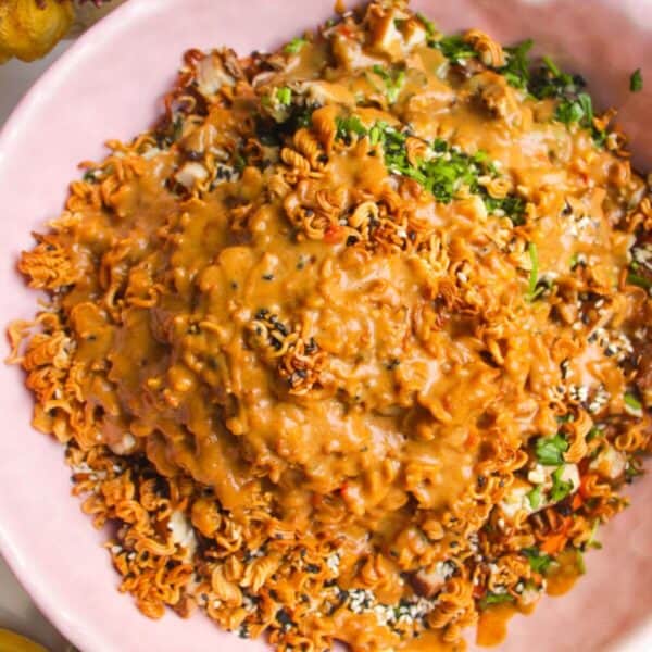Peanut satay dressing poured over crispy ramen salad in pink bowl.