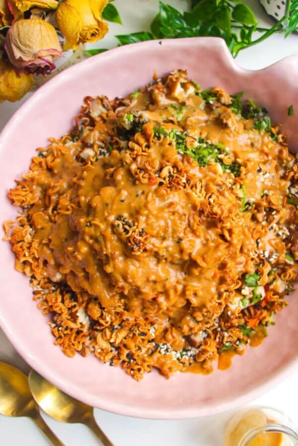 Peanut satay dressing poured over crispy ramen salad in pink bowl.