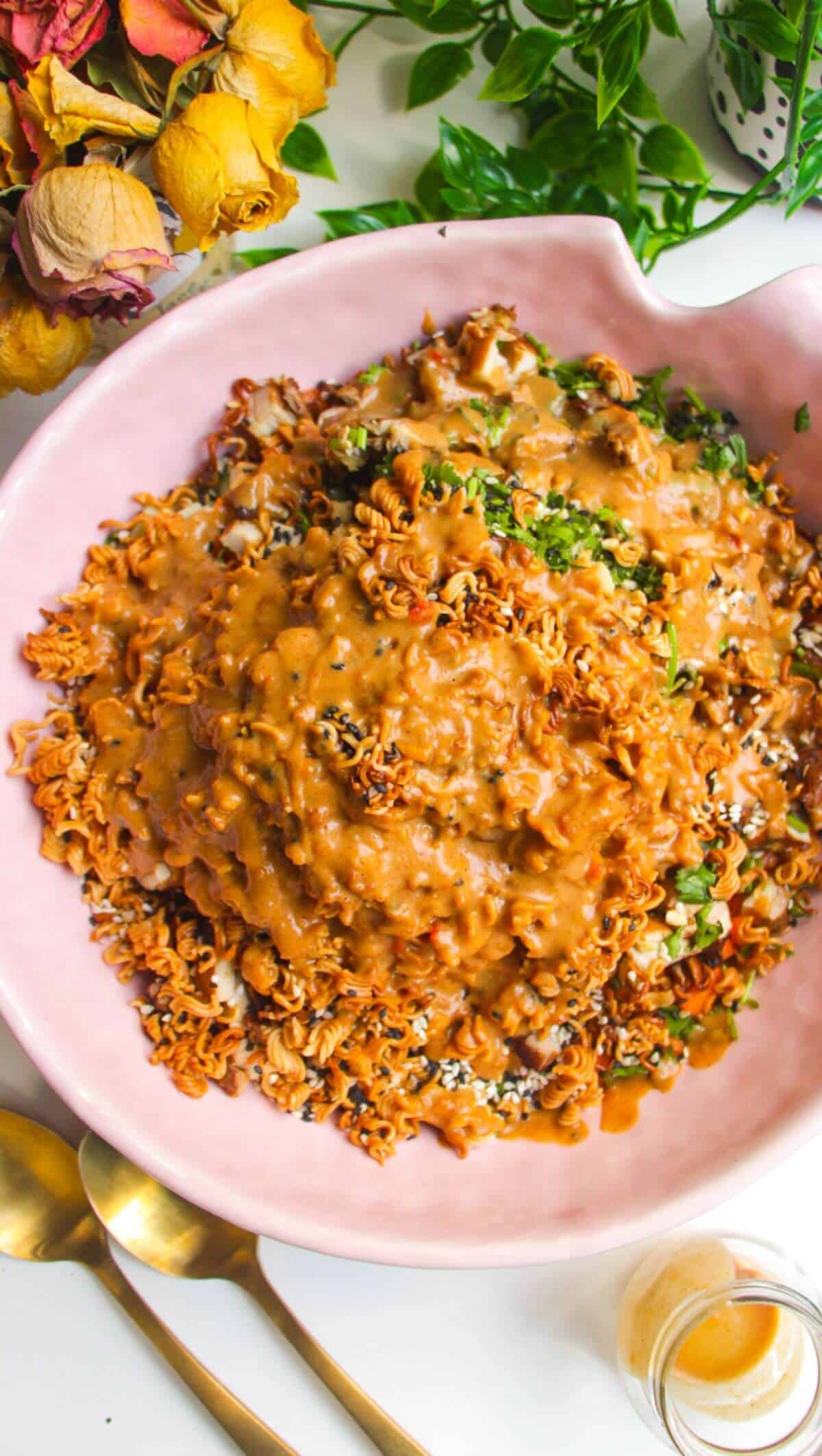 Peanut satay dressing poured over crispy ramen salad in pink bowl.