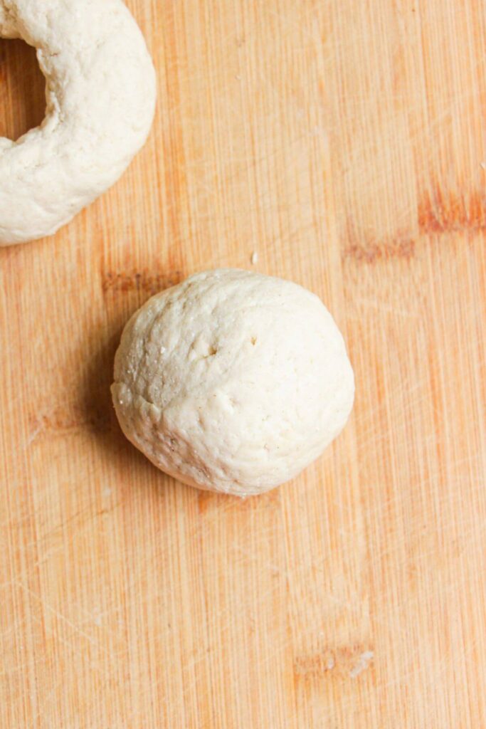 Bagel dough formed into a ball on wooden board.