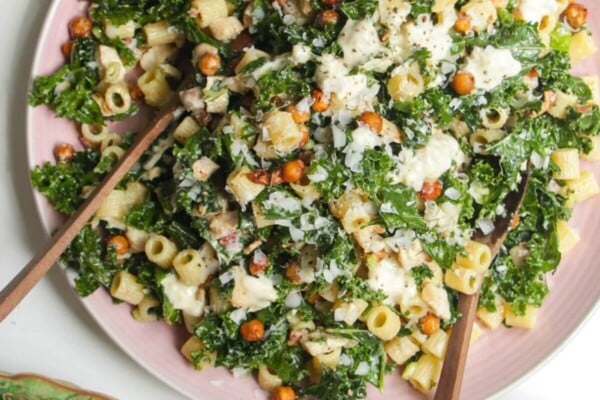 Chicken Caesar pasta salad in on a pink bowl with dressing on the side.