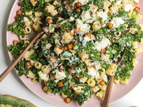 Chicken Caesar pasta salad in on a pink bowl with dressing on the side.