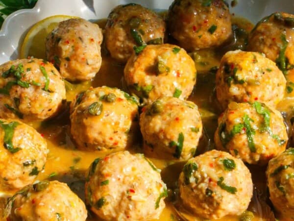 Chicken piccata meatballs in a white scalloped bowl.
