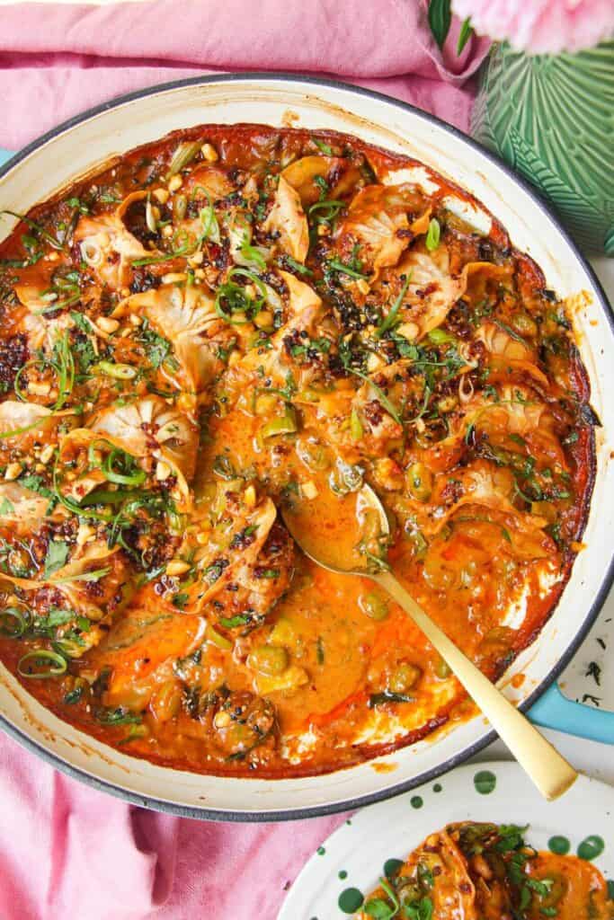 Baked dumplings in satay sauce in a skillet with chili oil on top.