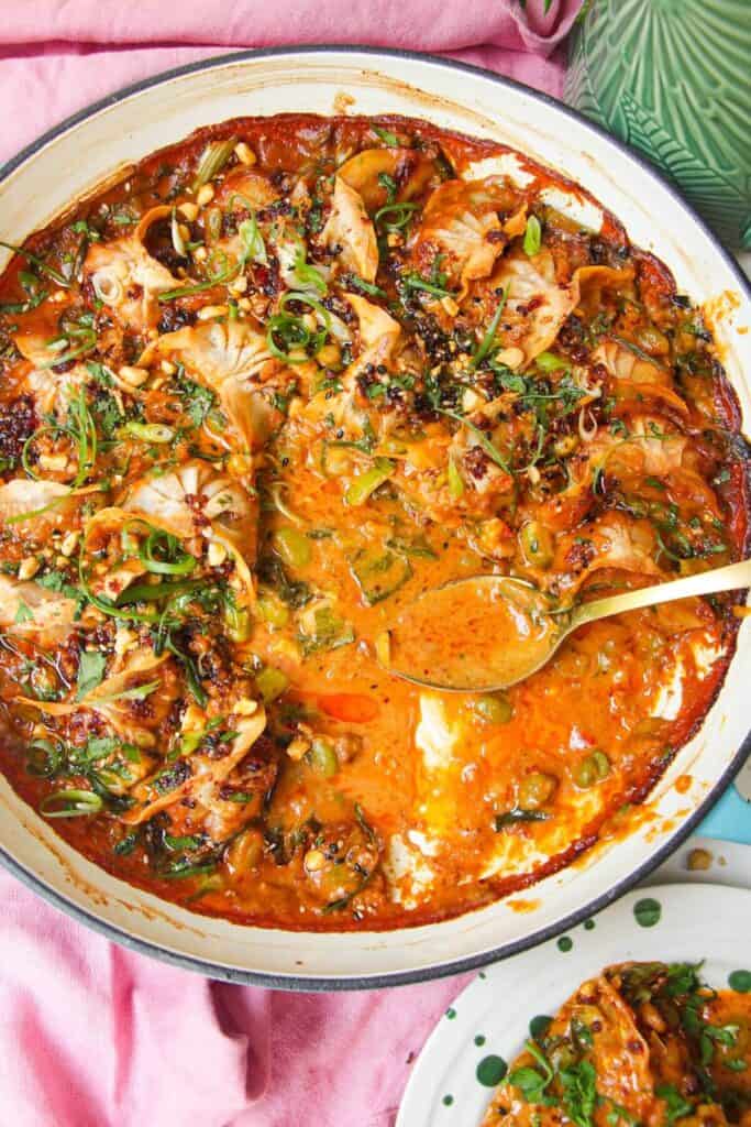Baked dumplings in satay sauce in a skillet with chili oil on top.