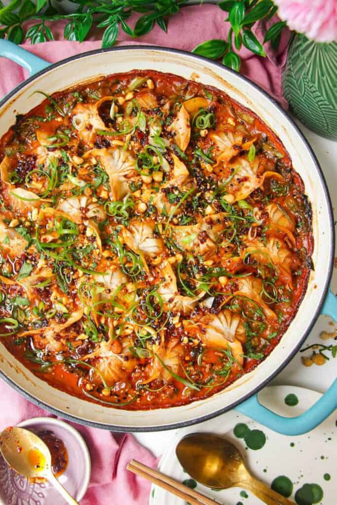 Baked dumplings in satay sauce in a skillet with chili oil on top.