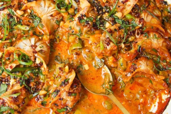 Baked dumplings in satay sauce in a skillet with chili oil on top.