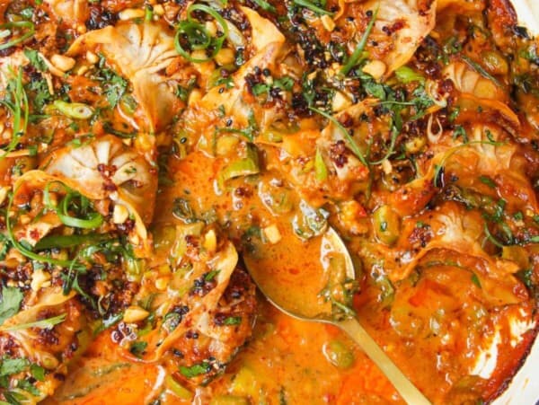 Baked dumplings in satay sauce in a skillet with chili oil on top.