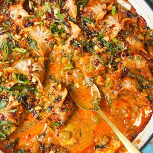 Baked dumplings in satay sauce in a skillet with chili oil on top.
