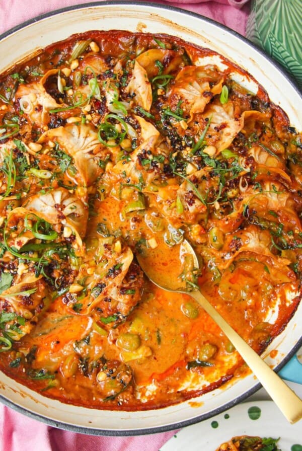 Baked dumplings in satay sauce in a skillet with chili oil on top.
