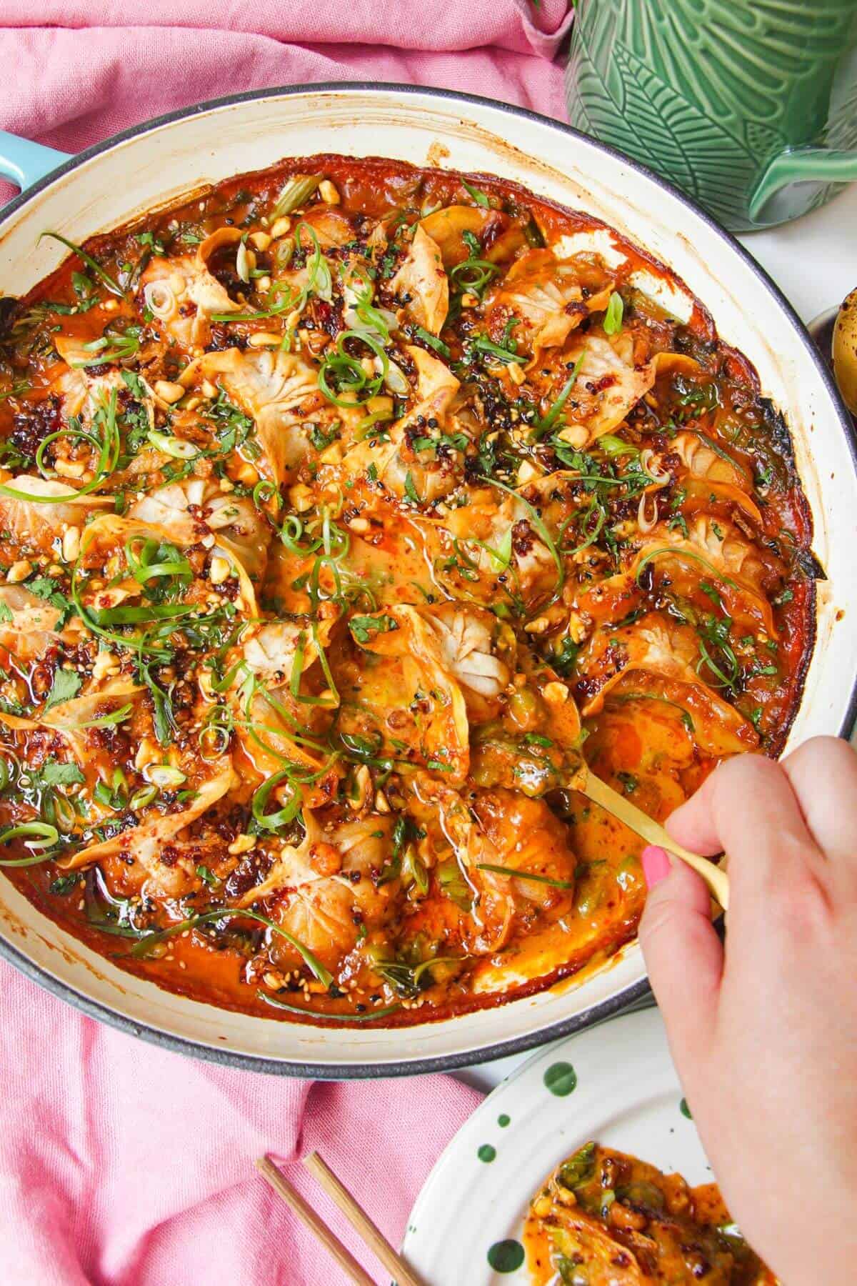 Baked dumplings in satay sauce in a skillet with chili oil on top.