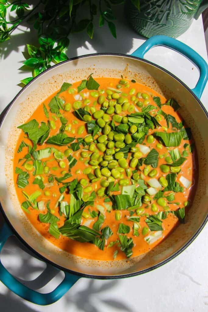 Edamame and bok choy scattered into sauce in pan.