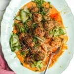 Dumpling meatballs on gochuajang sauce with pickled cucumber on an oval platter.